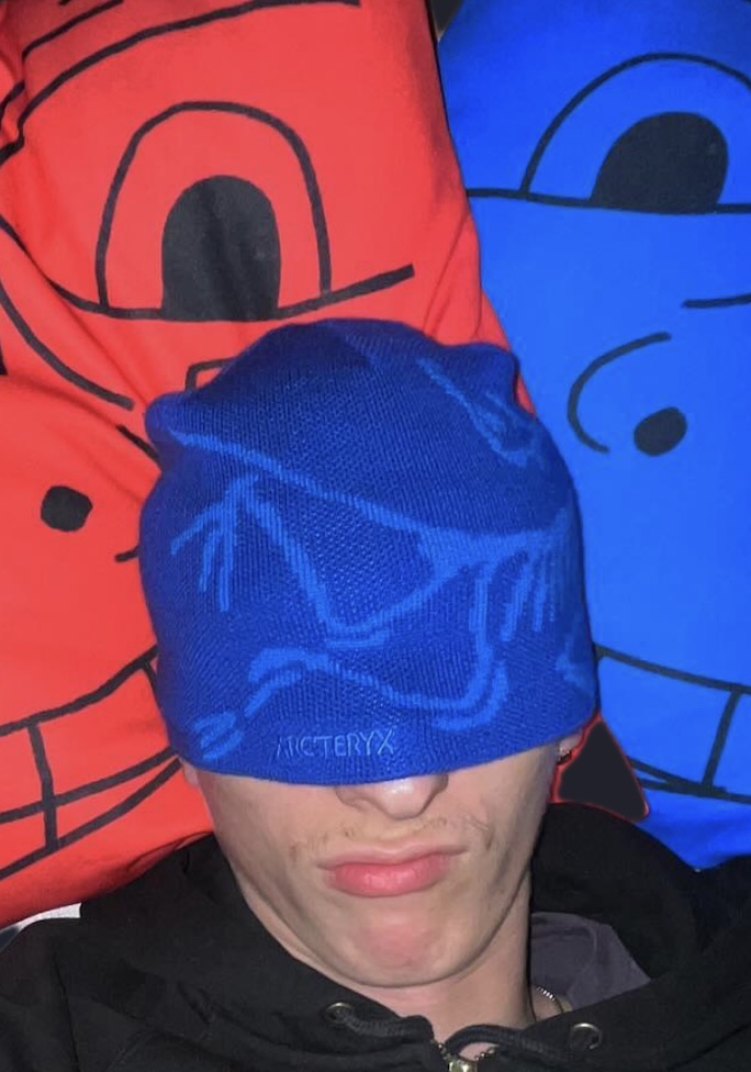 The maker behind atrostars wearing a blue Arc'teryx beanie, with the red and blue gremlin mascot pillows behind him